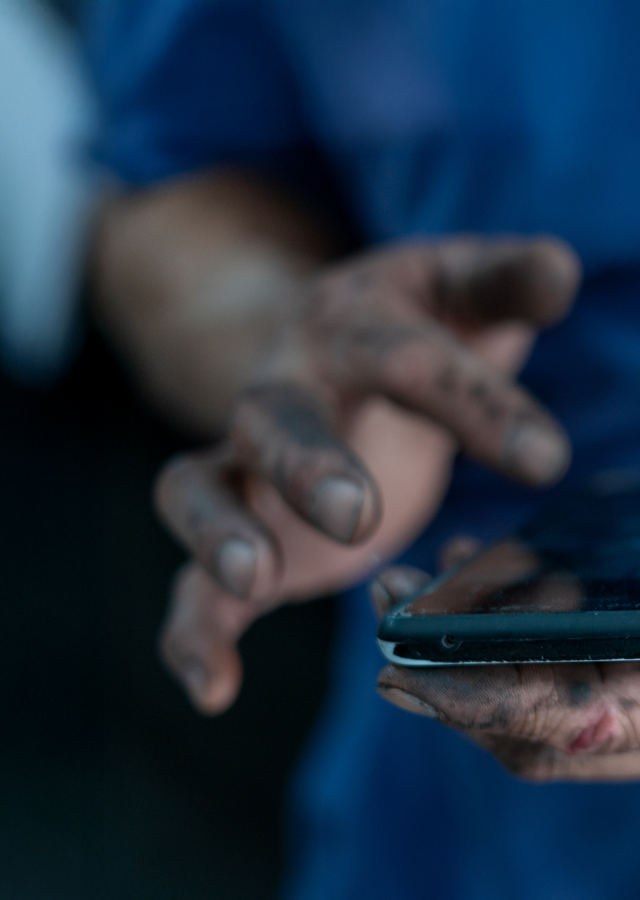 A mechanic's oily hands are doomscrolling, looking at the news on a phone.