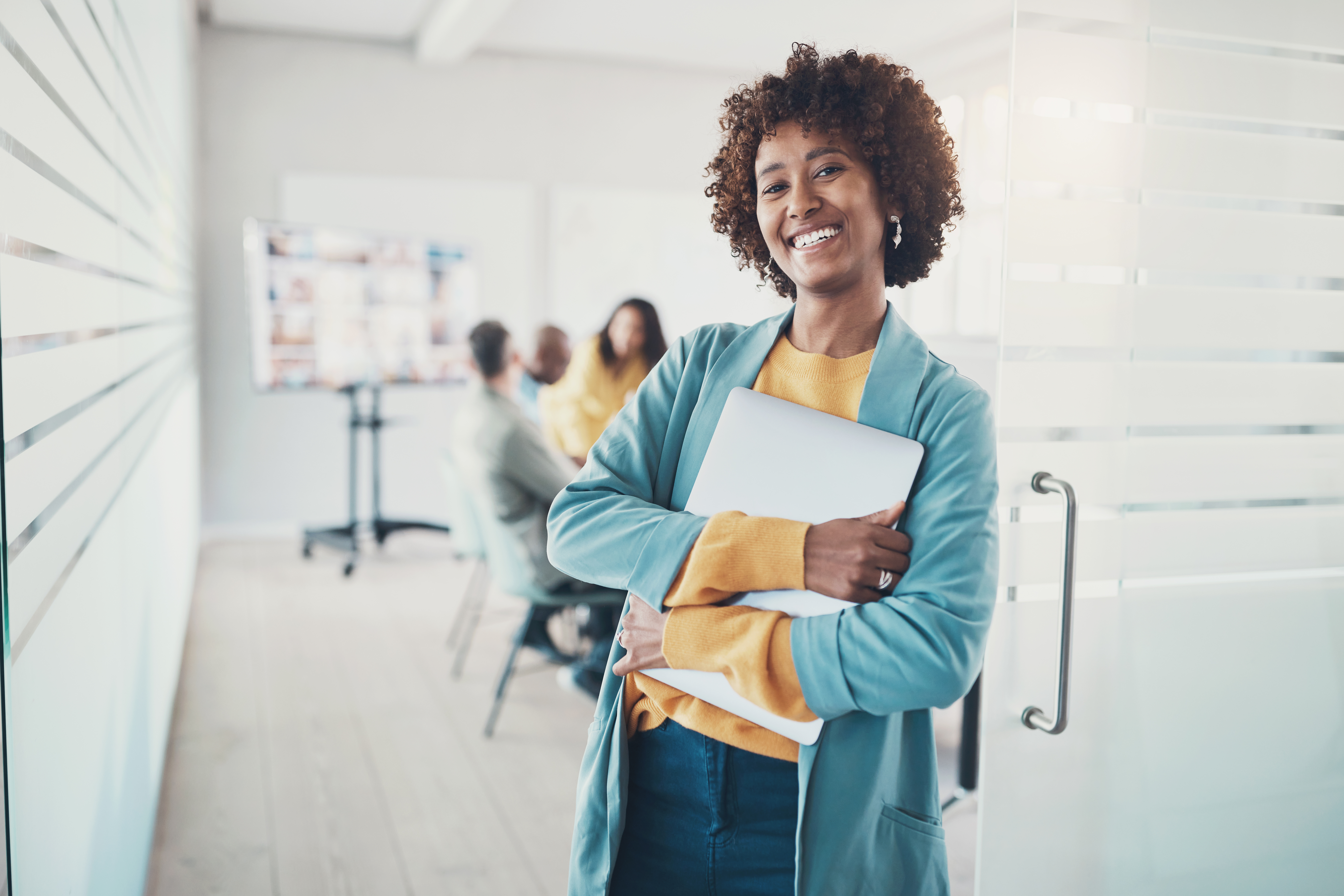 Smiling young businesswoman standing with a laptop before a boardroom meeting