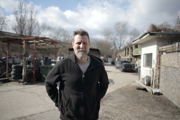A person standing outside in a car scrap yard looking towards the camera.