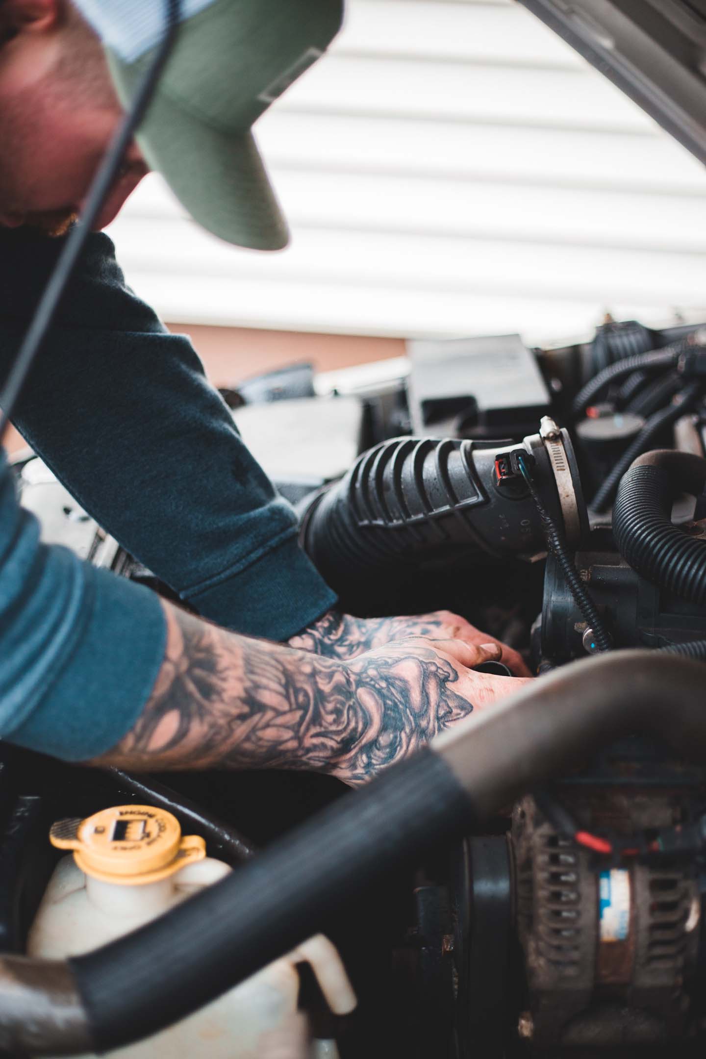 Tattooed vehicle technician fixing car engine considering changes in the industry and whether their job is at risk