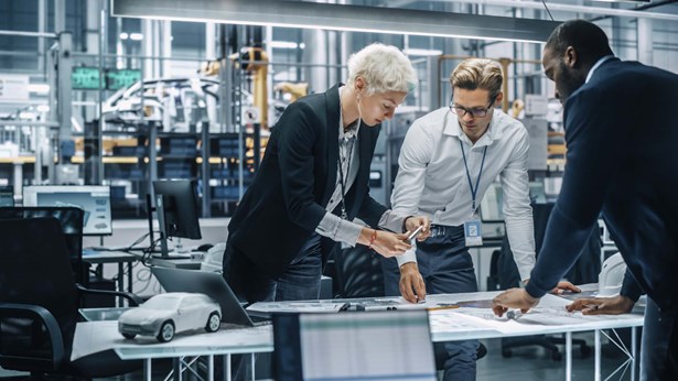 Team of automotive engineers working in office at car factory