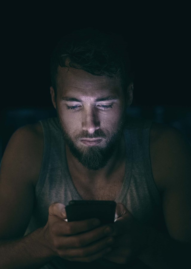 Person sitting in the dark looking at their smart phone