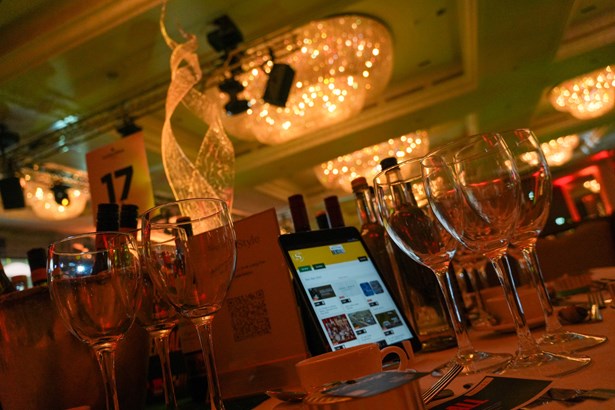 Close-up of wine glasses and a tablet on a table number 17 at a gala dinner, with chandeliers overhead.