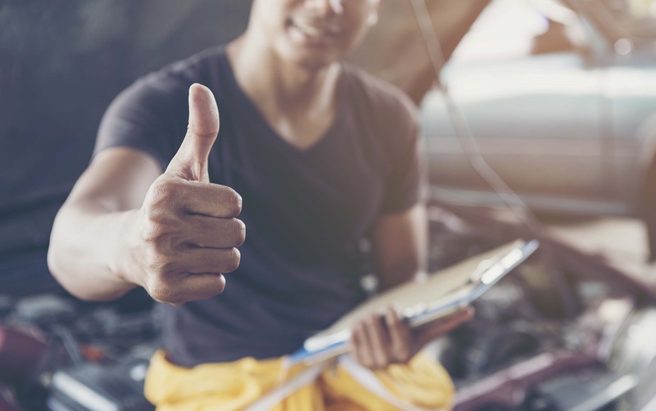 A person can on a car in a car workshop, happy with their thumbs up 