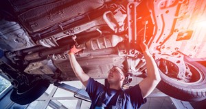 A smiling mechanic working on the underside of a car