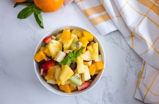 a bowl of mixed fruit salad with a sprig of mint as garnish