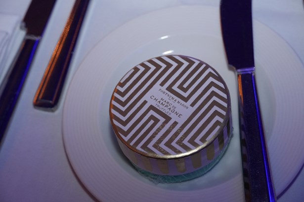 A round gift box of Fortnum & Mason Marc de Champagne truffles on a plate at a dinner table setting.