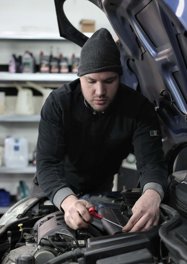 A mechanic working on a car engine by themselves