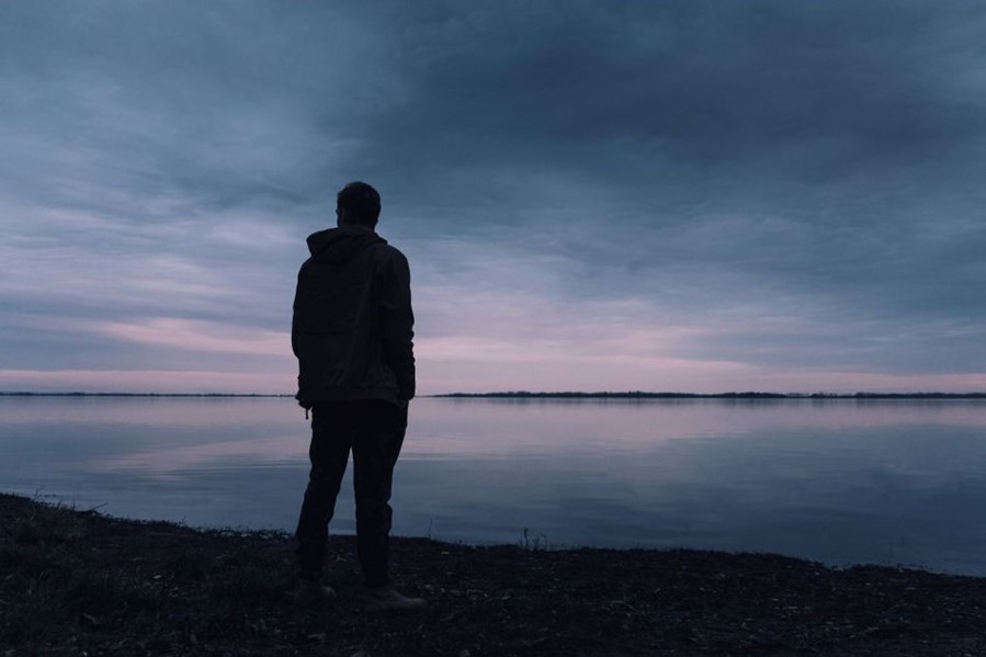 Lonely man standing beside a lake in late evening