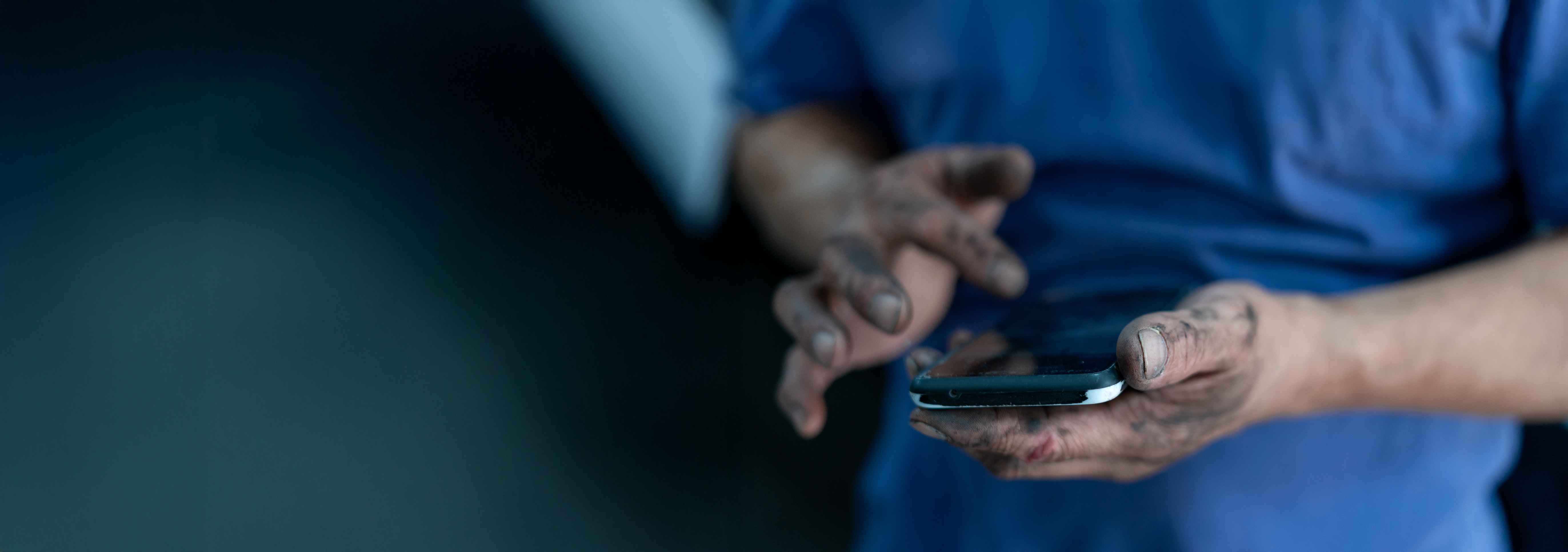 A mechanic's oily hands are doomscrolling, looking at the news on a phone. 