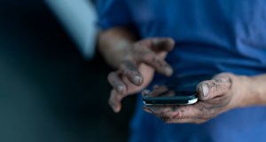 A mechanic's oily hands are doomscrolling, looking at the news on a phone.