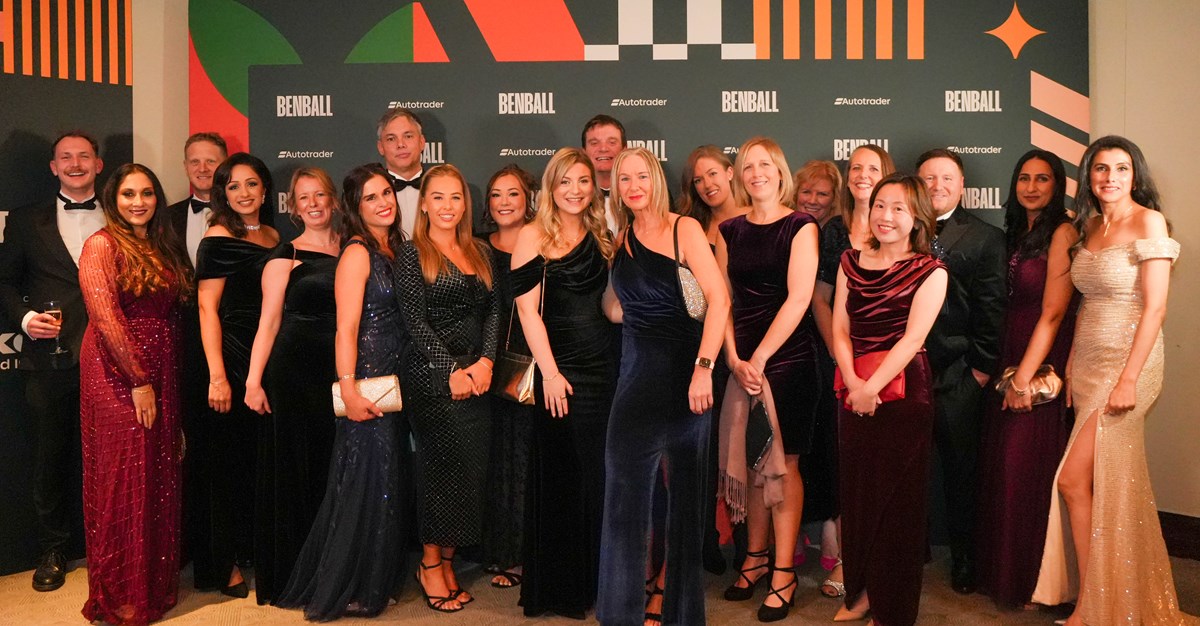 A large group of guests in black tie and evening gowns posing in front of the Ben Ball and Autotrader branded backdrop.
