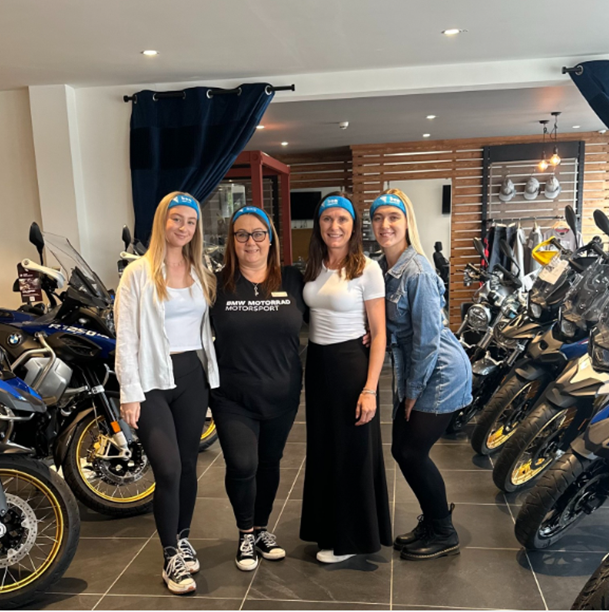 Four colleagues wearing blue Ben headbands pose together in a motorcycle showroom.