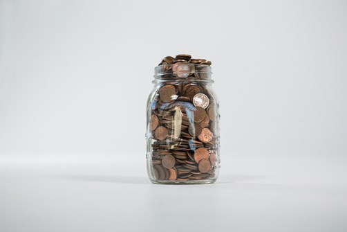 A glass jar filled to the brim with copper coins on a plain white background.