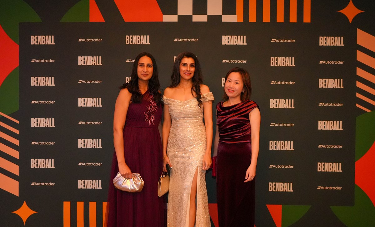 Three guests in evening gowns pose in front of the BenBall and Autotrader branded backdrop.