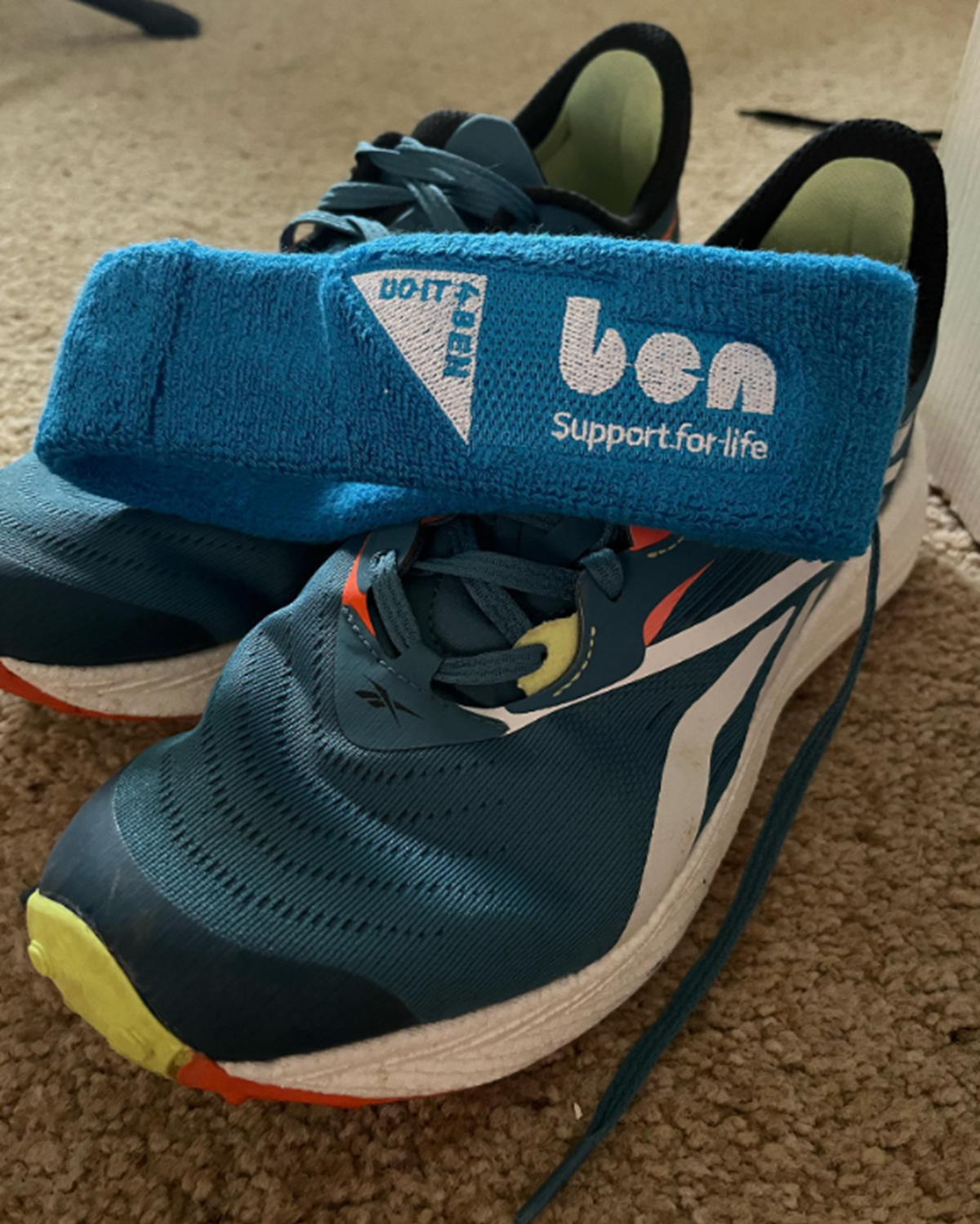 Blue 'ben - support for life' sweatband resting on a pair of running trainers.