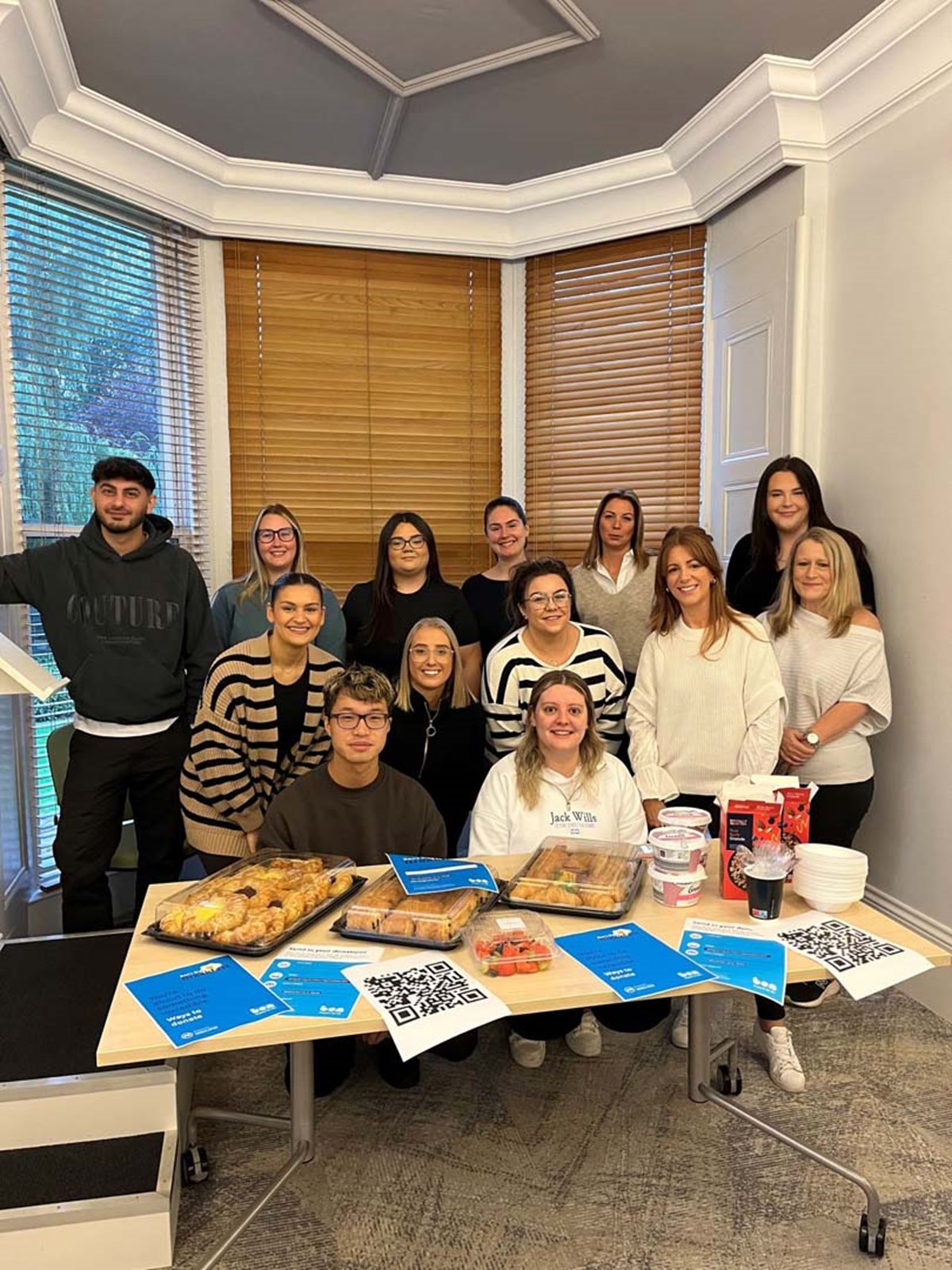 A team of colleagues gathered in an office around a table laid with pastries, fruit and Ben leaflets for Ben's Big Breakfast.