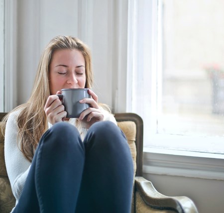 A person enjoying hot drink legs curled up on chair on a winter's afternoon. Self-care, looking after yourself and managing your own wellbeing