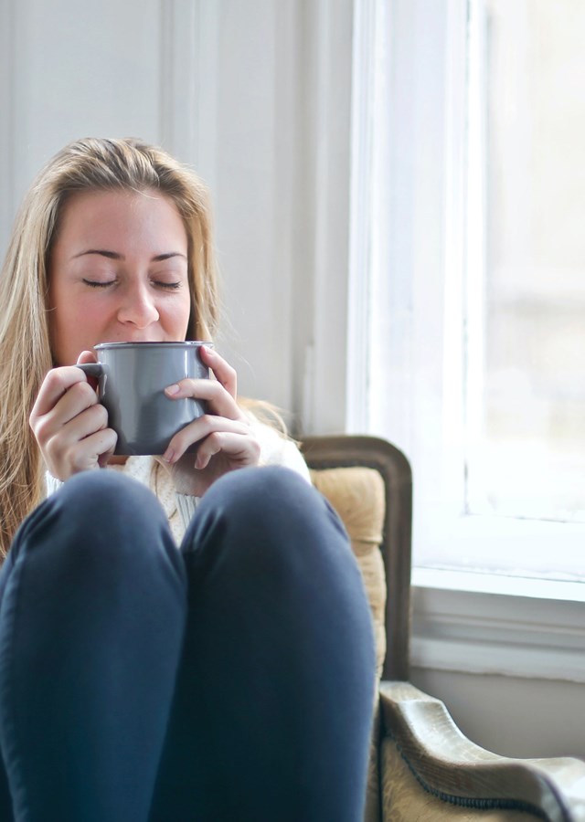 A person enjoying a hot drink with their legs curled up on chair on a wet afternoon. 