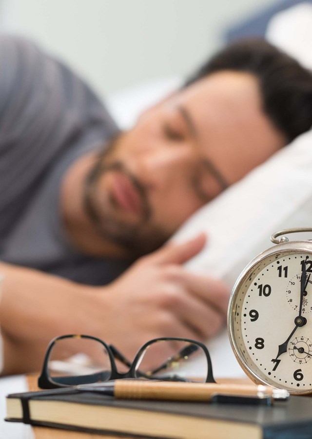 Man asleep about to be awakened by alarm clock. Learn how to get good sleep with these tips. Getting good rest is good for your health and wellbeing