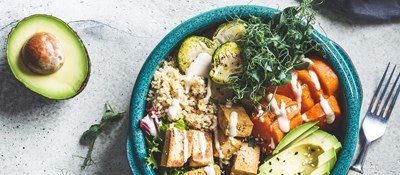 A large blue bowl full of colourful healthy food sitting on a table with a fork to one side and half an avocado on the other