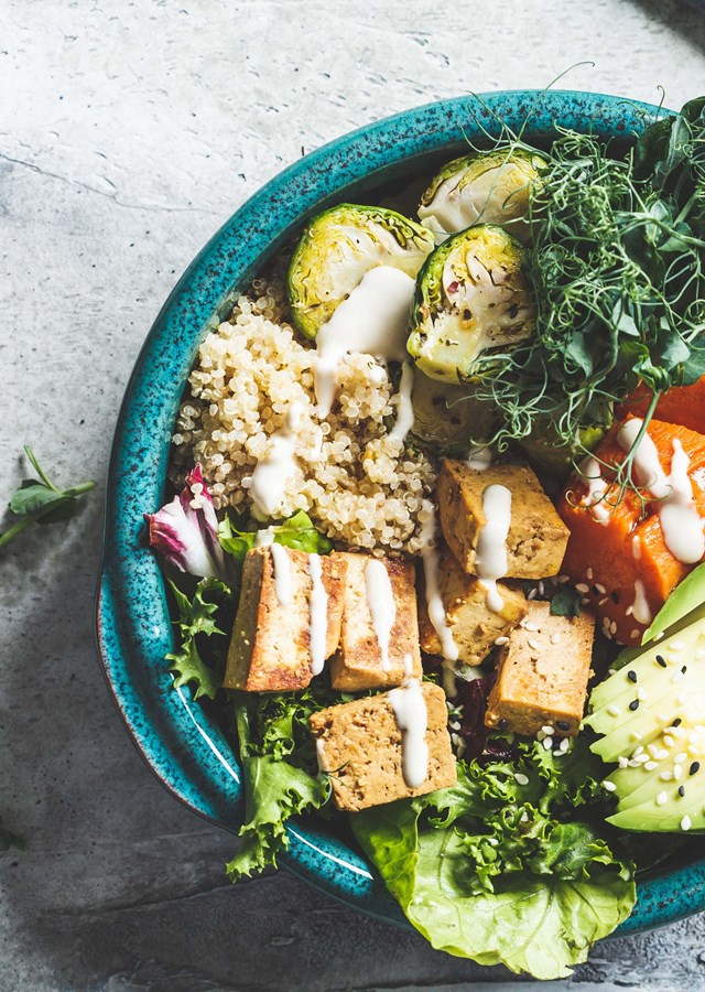 A large blue bowl full of colourful healthy food sitting on a table with a fork to one side and half an avocado on the other