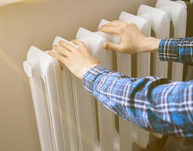 A person in a checked shirt warming their hands on a white radiator