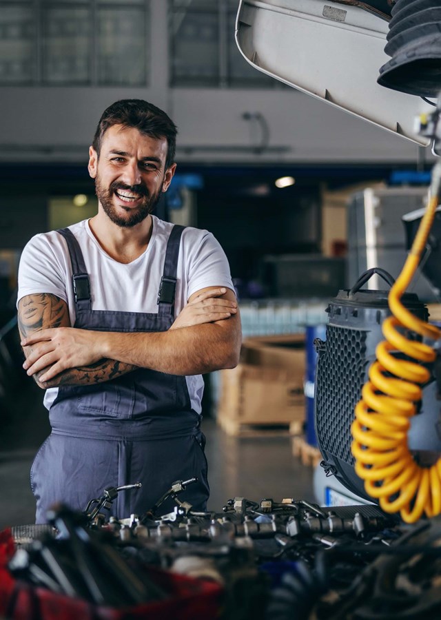 A smiling mechanic (vehicle technician) standing in a garage next to a truck being repaired