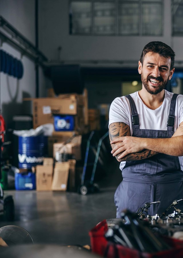 A smiling mechanic (vehicle technician) standing in a garage next to a truck being repaired