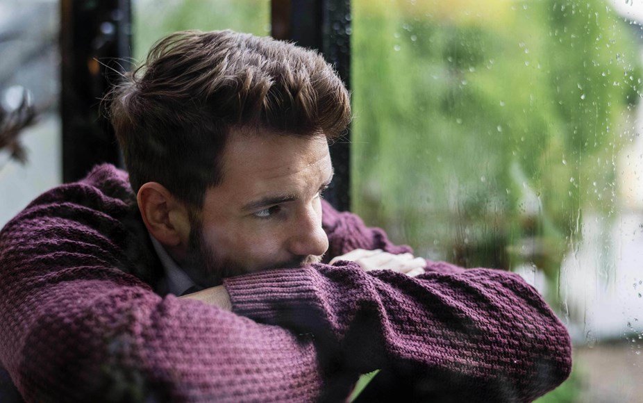 Person resting their chin on crossed arms looking out a window on a rainy day