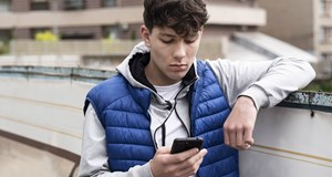 A person looking at their smart phone concerned, while leaning on a wall