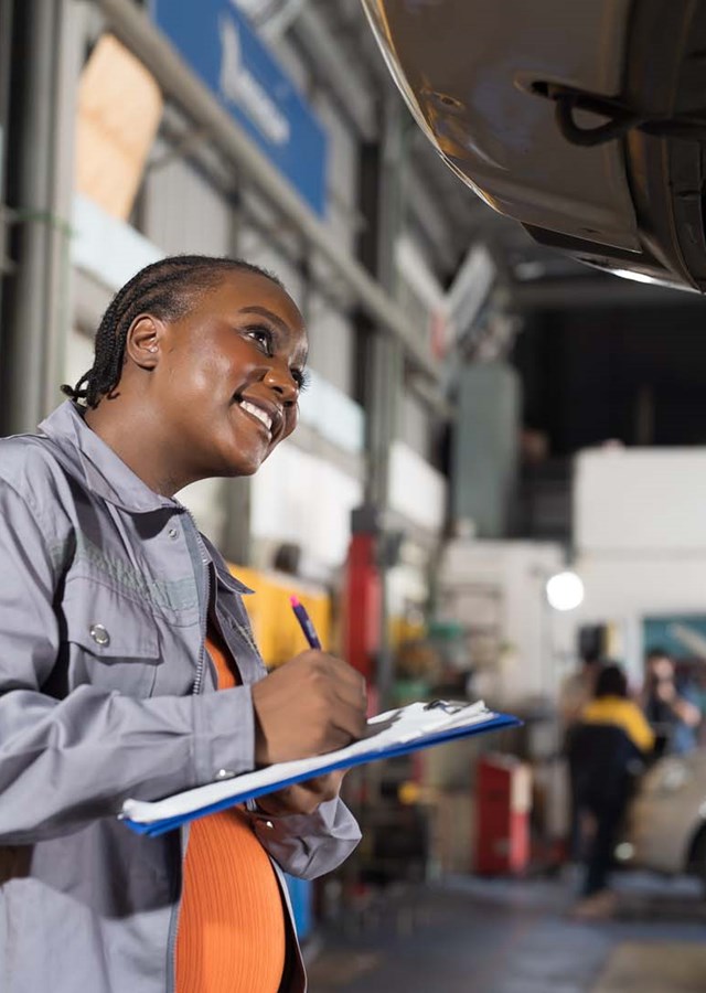 Female mechanic checking car engine underneath a car on a lift at auto car repair service. 