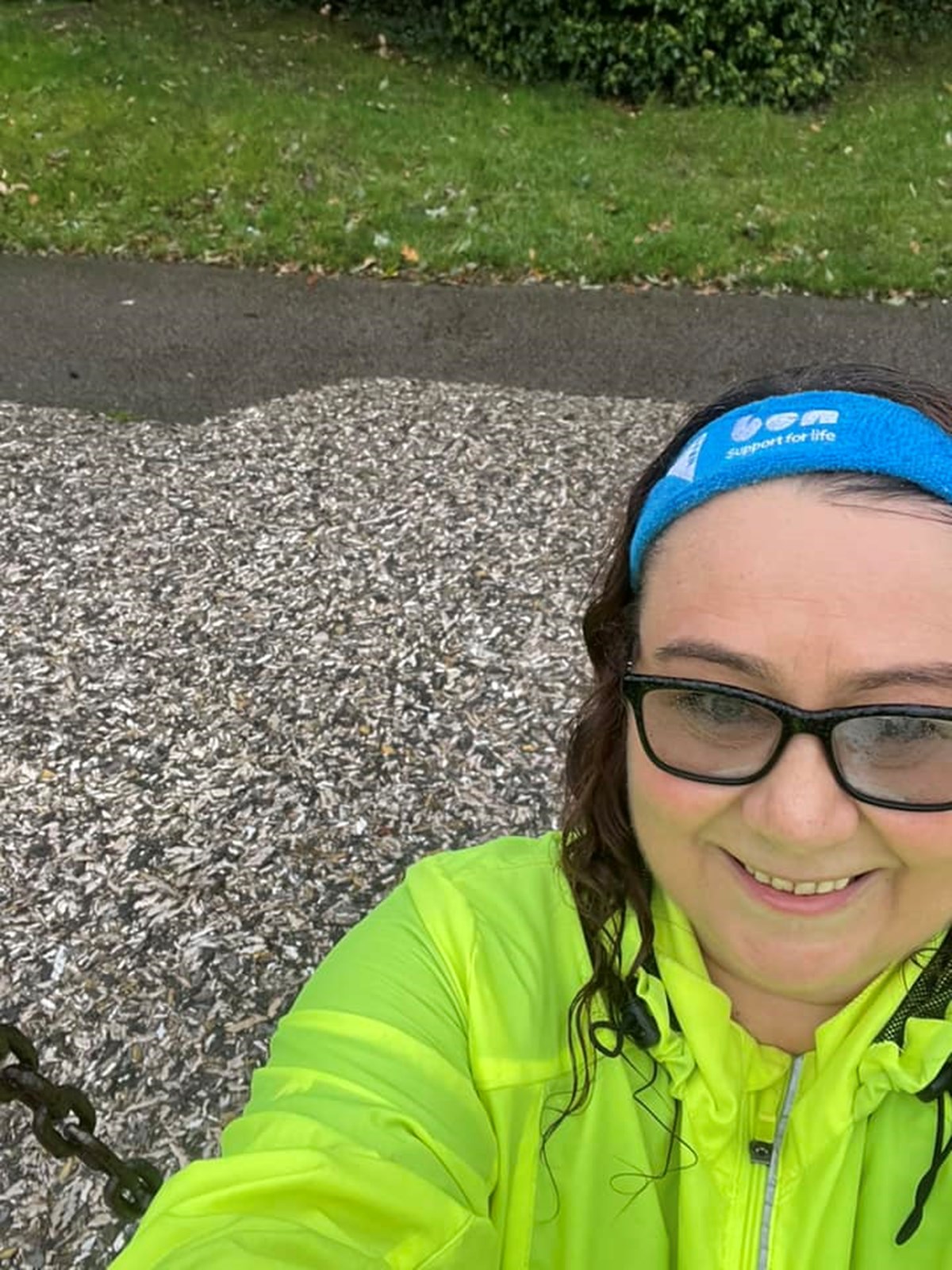 Smiling woman in a hi-vis jacket and blue Ben 'Support for life' headband taking a selfie outdoors on a path.