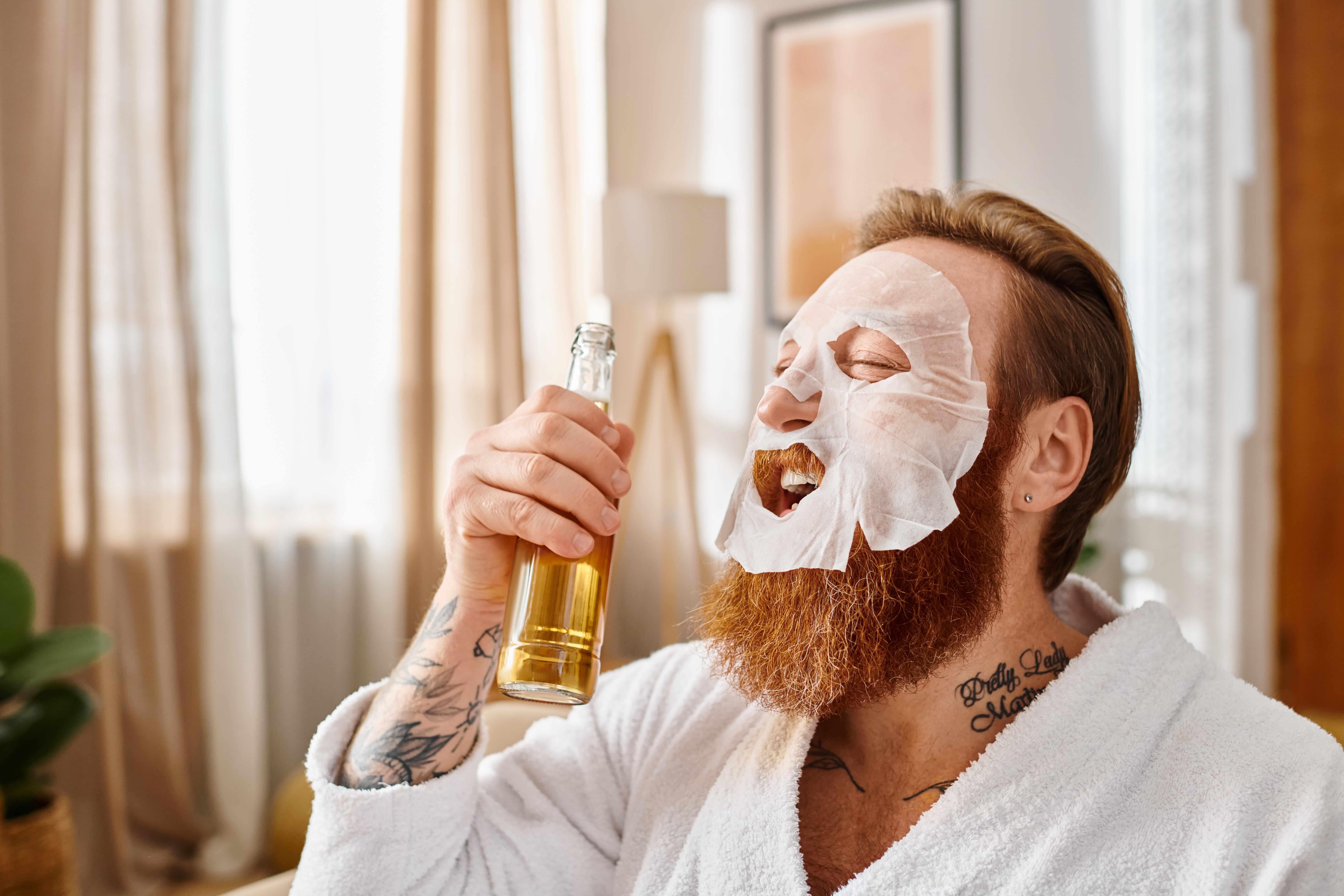 A man in a facial mask holds a bottle of drink, embodying relaxation and self-care while enjoying a moment of indulgence.