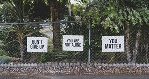 Three white signs, saying,' don't give up', 'you are not alone' and 'you matter', attached to a metal fence