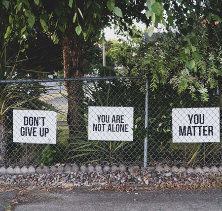 Three white signs, saying,' don't give up', 'you are not alone' and 'you matter', attached to a metal fence