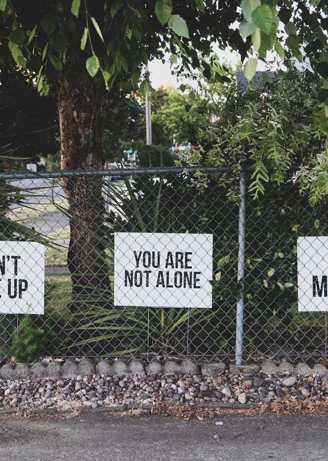 Three white signs, saying ,'don't give up', 'you are not alone' and 'you matter', attached to a metal fence