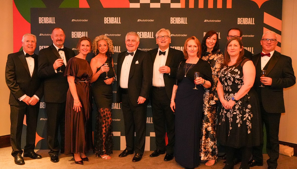 A group of guests in black tie and evening dresses holding drinks in front of a Ben Ball and Autotrader branded backdrop.