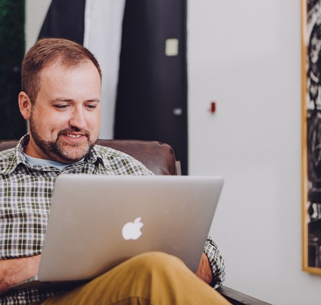 Man sitting comfortably in an armchair with his laptop, smiling