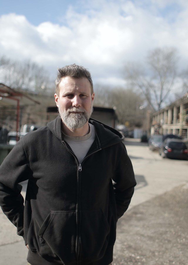 A person standing outside in a car scrap yard looking towards the camera.