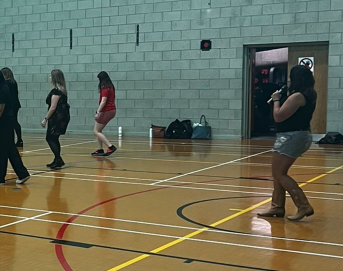 A group of women taking part in a line dancing class in a sports hall.