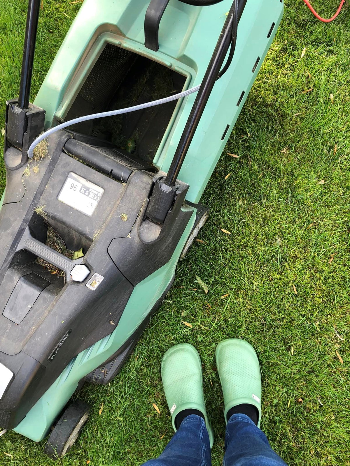 Looking down at a pair of green wellies on a freshly mown lawn beside a green electric lawnmower.