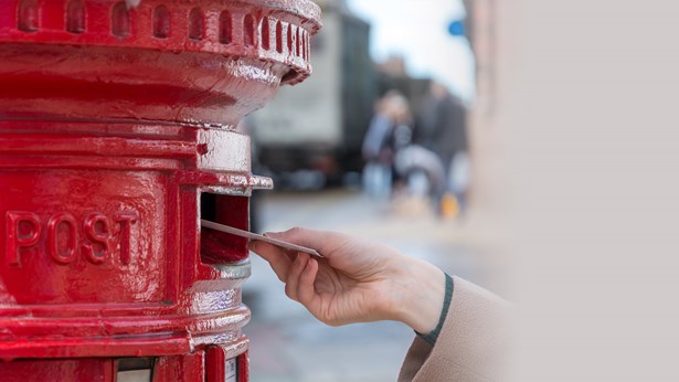Hand posting letter in to a red post box