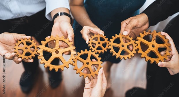 A group of colleagues each holding a wooden cog, connected together to form a chain.