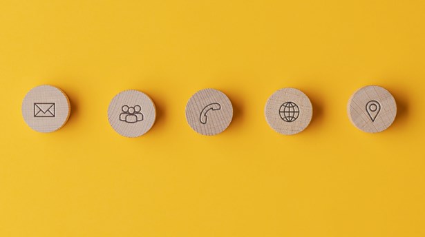 Five wooden discs on a yellow background showing contact icons: envelope, people, telephone, globe and location pin.