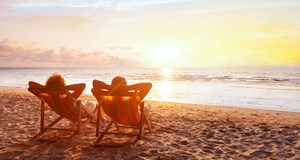 Two people enjoying their retirement sitting on deckchairs on a beach, watching the sunset