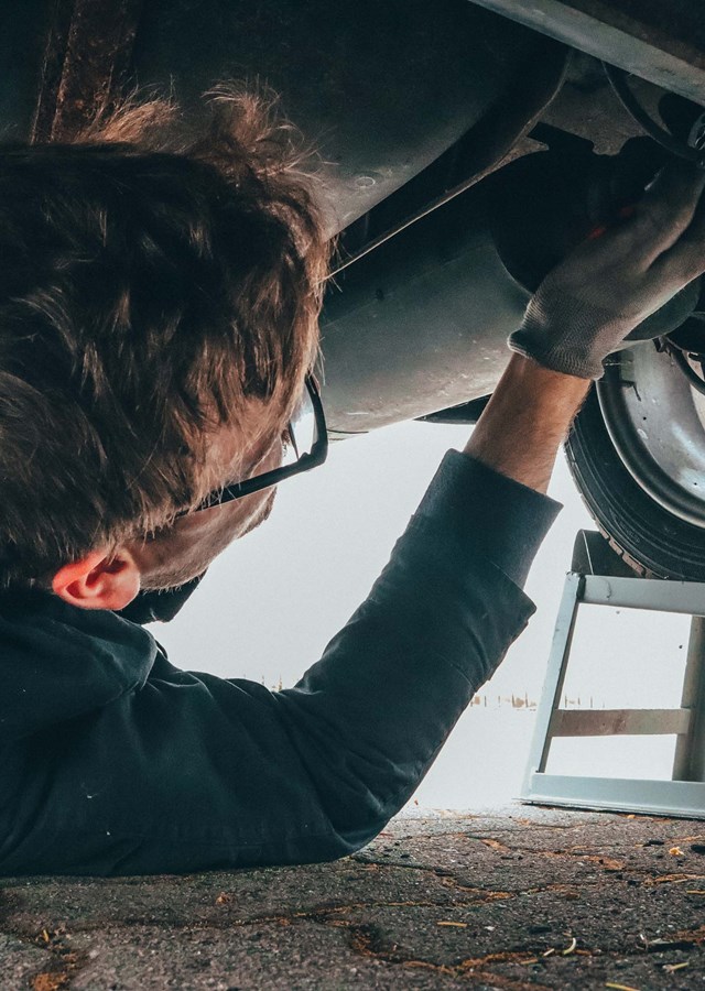 A mechanic (vehicle technician) lying on the floor working on the under side of a car