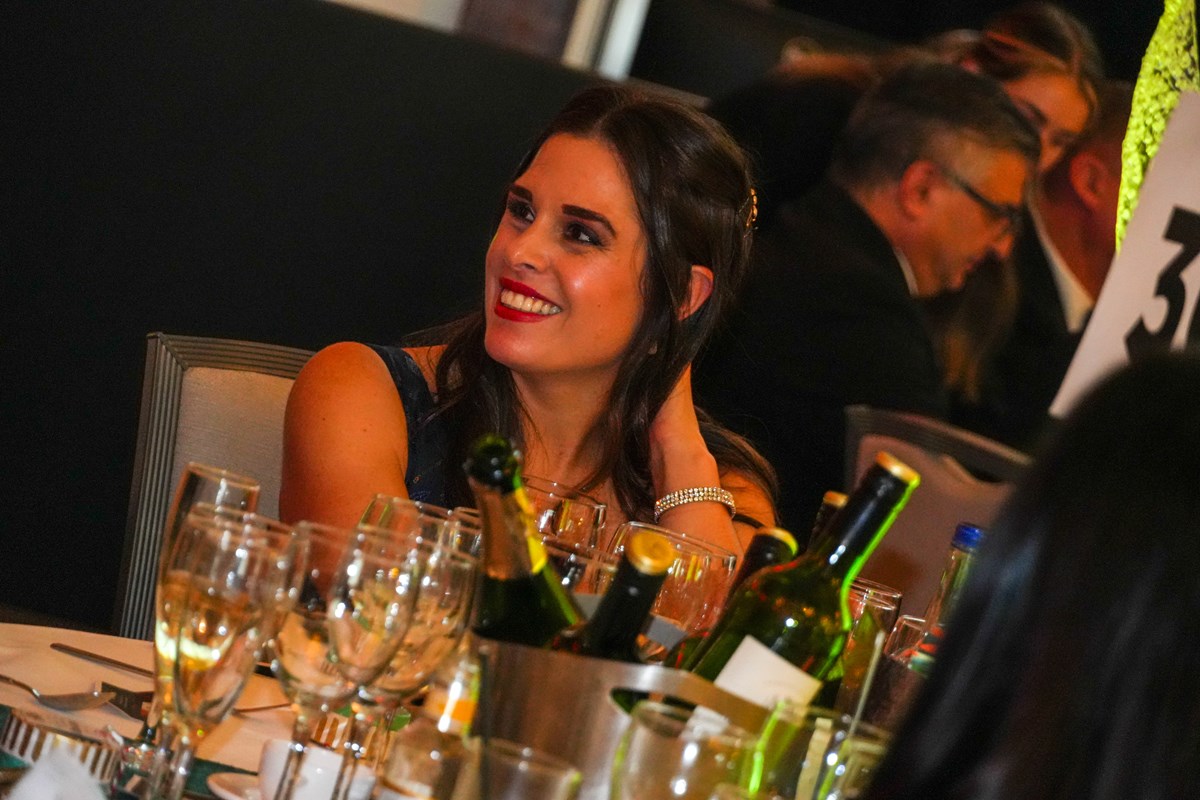 A guest smiles at her table at Ben Ball, with wine bottles and glasses in the foreground.