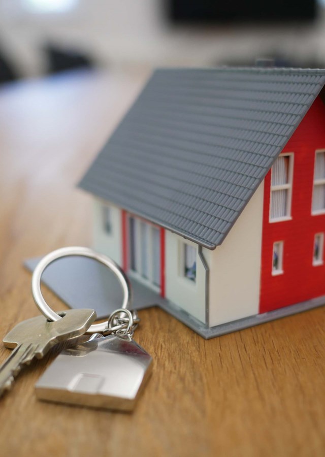A small red and white 3D house on a key ring with a house key attached, sitting on a table