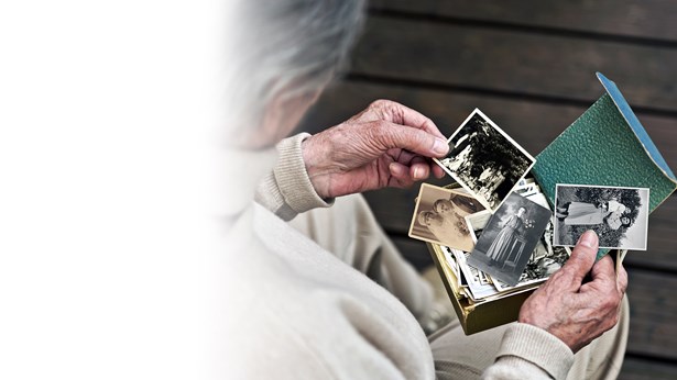 An older woman holding a box of old black and white family photographs, looking through them.